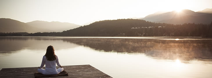 woman sitting on a dock in the middle of a lake while the sun rises
